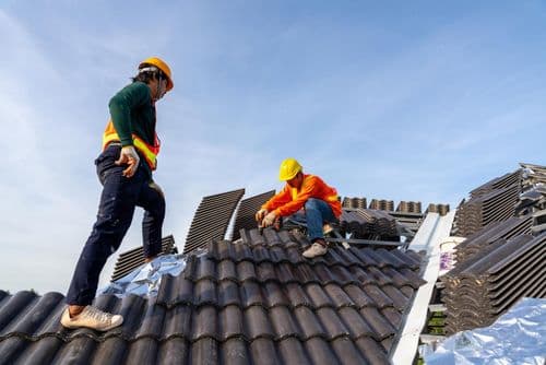 Two roofing technicians actively installing roofing materials on a residential roof