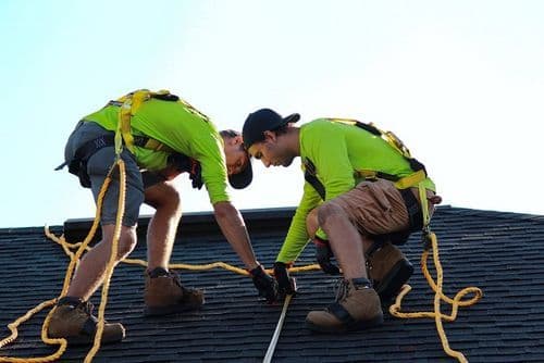 Two roofers in safety harnesses working on an Arlington TX residential roof